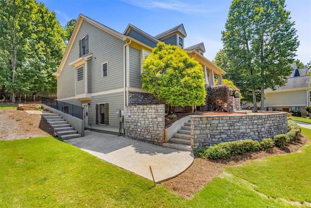 rear view of property featuring a yard, stairs, and a patio