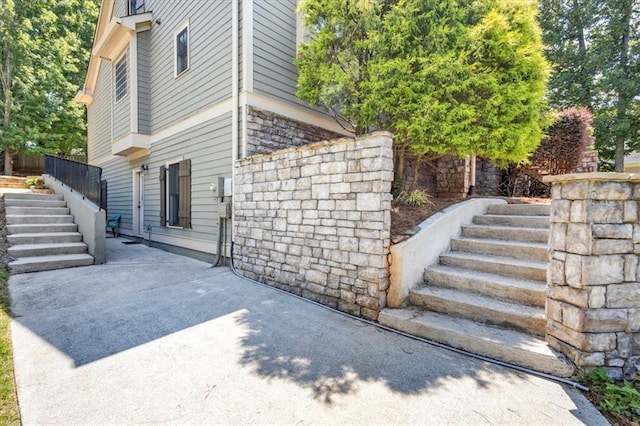view of side of home featuring stone siding, stairway, and a patio