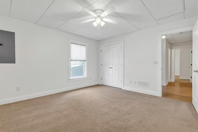 unfurnished bedroom with carpet flooring, baseboards, a drop ceiling, visible vents, and electric panel