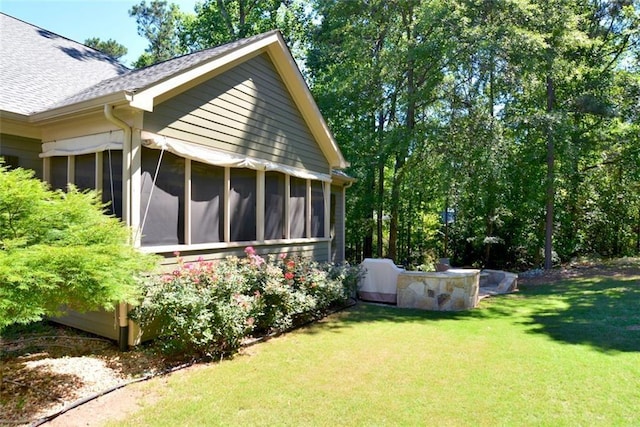view of home's exterior with a sunroom, roof with shingles, and a yard