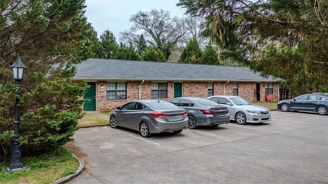 view of front of house featuring brick siding, a shingled roof, and uncovered parking