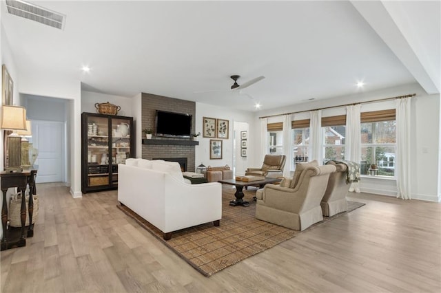 living room featuring ceiling fan, a fireplace, and light hardwood / wood-style floors