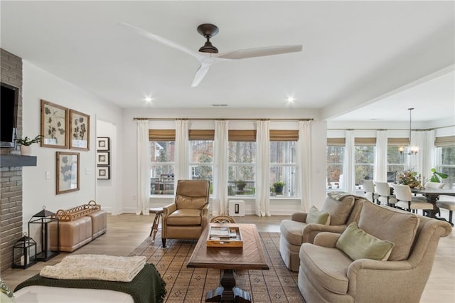 living room with a brick fireplace, ceiling fan with notable chandelier, and light hardwood / wood-style flooring