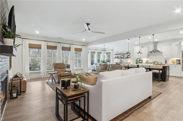 living room featuring ceiling fan, a brick fireplace, and light hardwood / wood-style flooring