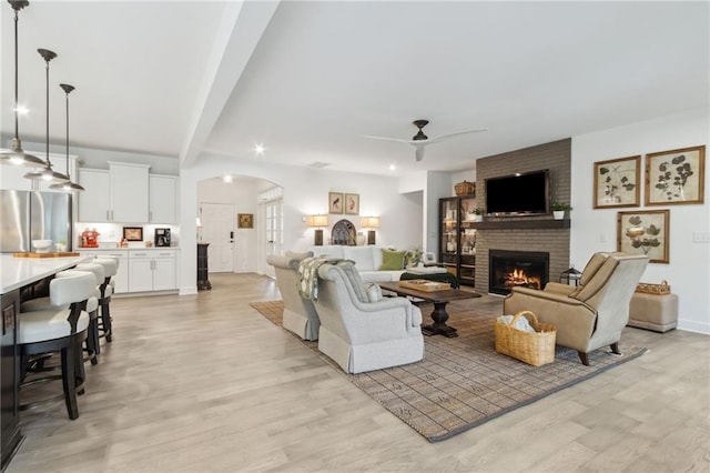 living room with beamed ceiling, ceiling fan, a fireplace, and light wood-type flooring