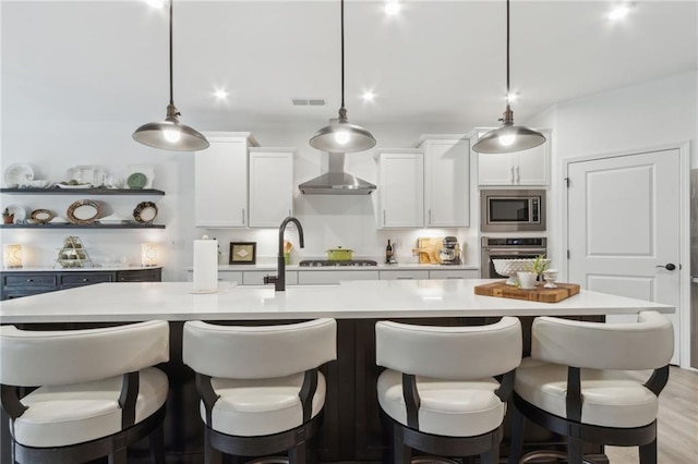 kitchen featuring white cabinetry, hanging light fixtures, an island with sink, and appliances with stainless steel finishes