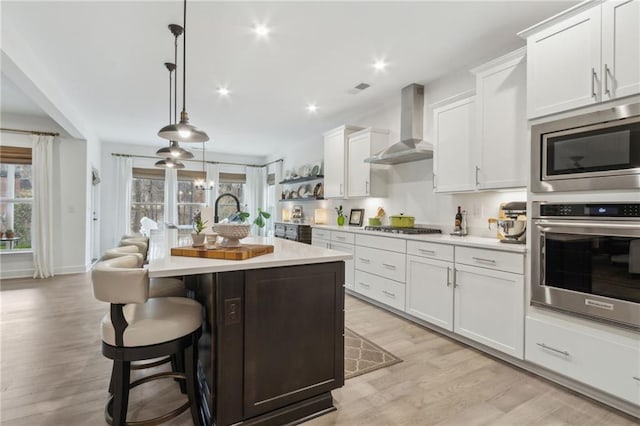 kitchen with white cabinets, wall chimney exhaust hood, and a center island with sink