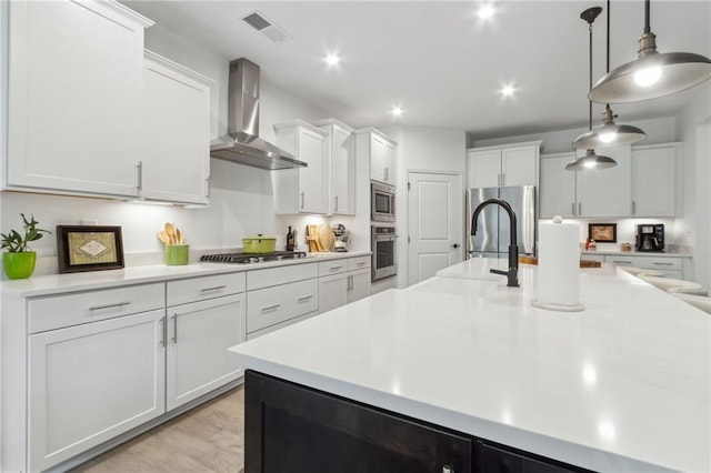 kitchen with stainless steel appliances, white cabinetry, decorative light fixtures, and wall chimney exhaust hood