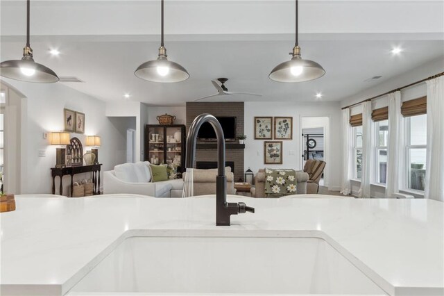 interior space with hanging light fixtures, a brick fireplace, sink, and ceiling fan