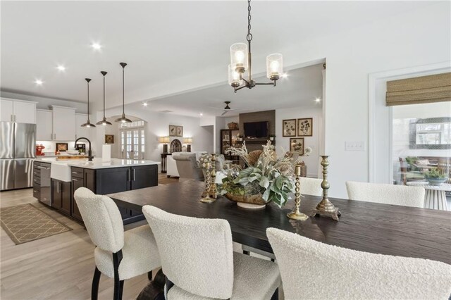 dining area with ceiling fan with notable chandelier, sink, and light wood-type flooring