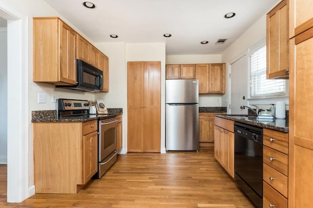 kitchen with a sink, visible vents, light wood-type flooring, dark stone counters, and black appliances