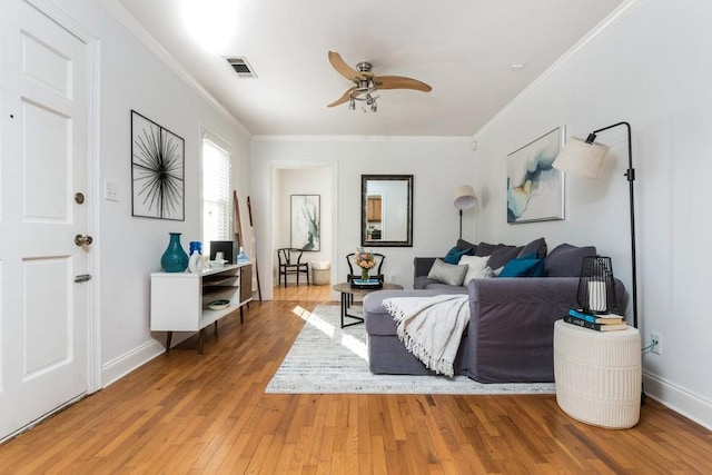 living room featuring ceiling fan, wood finished floors, visible vents, baseboards, and ornamental molding