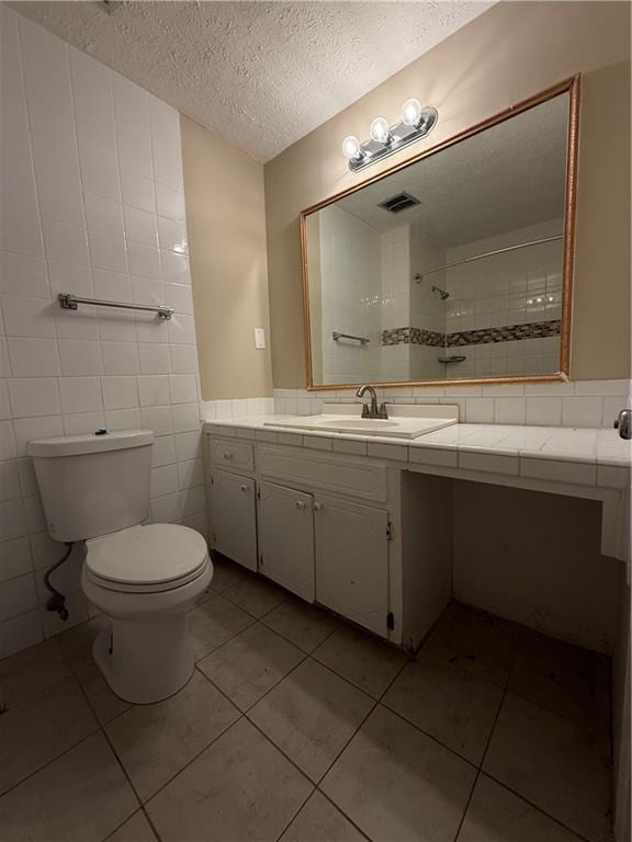 full bath with vanity, toilet, a textured ceiling, visible vents, and tiled shower