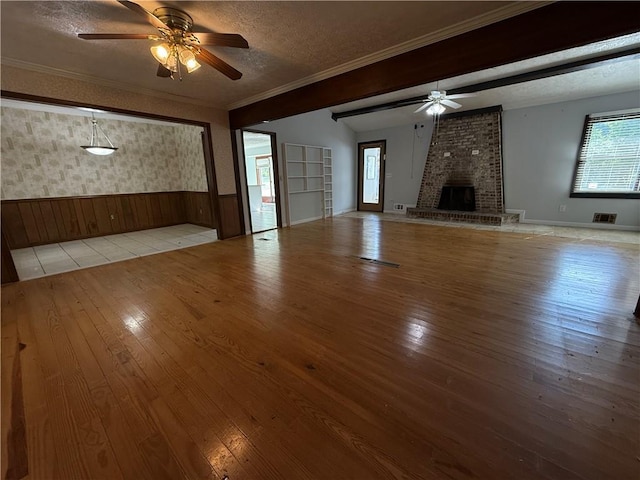 unfurnished living room featuring a textured ceiling, plenty of natural light, a wainscoted wall, hardwood / wood-style floors, and a ceiling fan