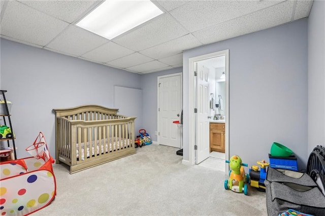 carpeted bedroom with ensuite bathroom, a drop ceiling, and a crib