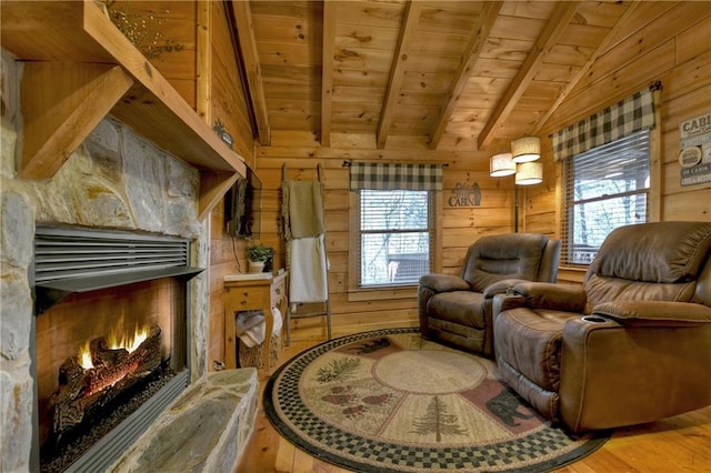 living area featuring wooden walls, a healthy amount of sunlight, vaulted ceiling with beams, wood ceiling, and a warm lit fireplace