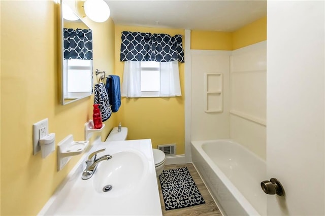 bathroom with toilet, baseboards, a sink, visible vents, and wood finished floors