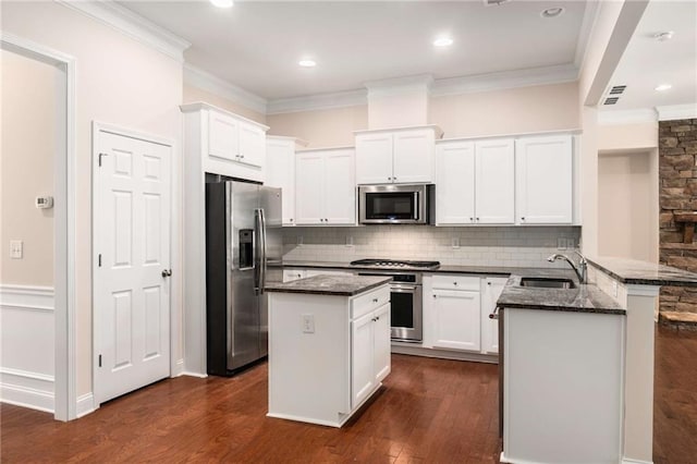 kitchen featuring a center island, kitchen peninsula, dark stone countertops, white cabinetry, and stainless steel appliances