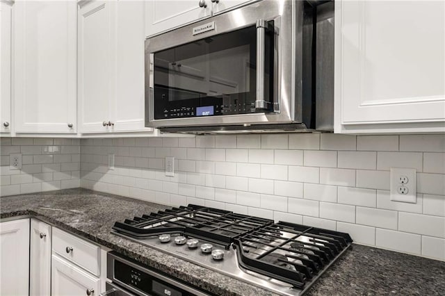 kitchen with white cabinets, backsplash, stainless steel appliances, and dark stone counters