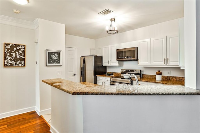 kitchen featuring kitchen peninsula, appliances with stainless steel finishes, dark stone counters, white cabinets, and light hardwood / wood-style floors