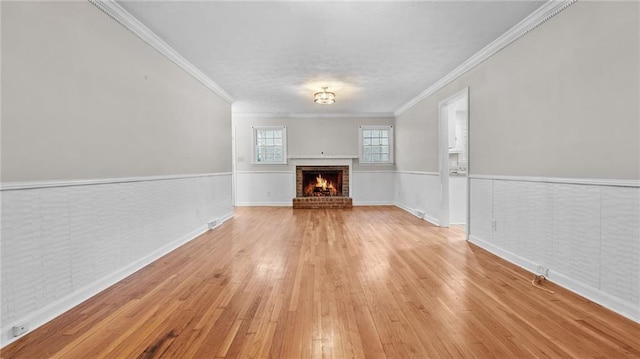 unfurnished living room with light wood-style floors, a brick fireplace, a wainscoted wall, and crown molding