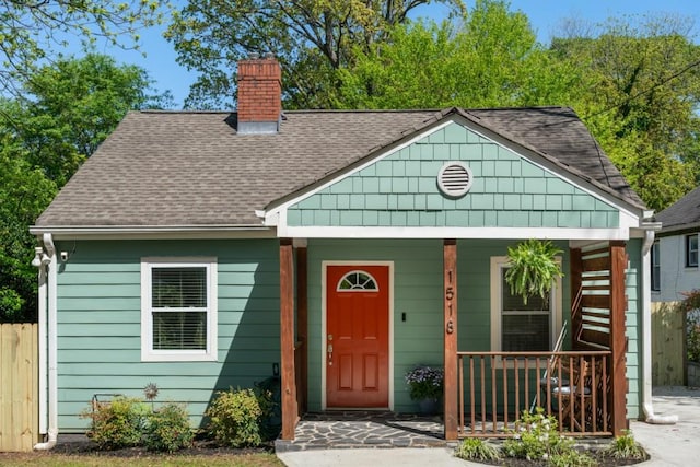 view of front of home with a porch, roof with shingles, fence, and a chimney