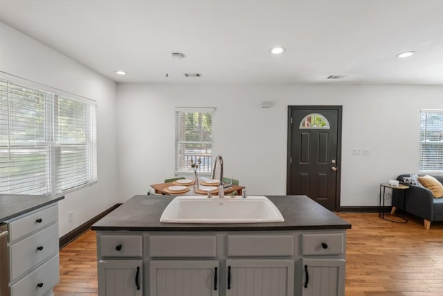 kitchen featuring light wood-style flooring, a sink, dark countertops, visible vents, and recessed lighting