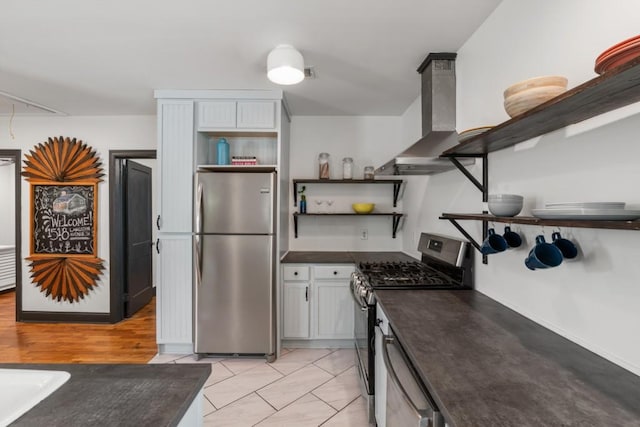 kitchen featuring open shelves, dark countertops, appliances with stainless steel finishes, and wall chimney range hood