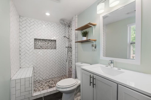 full bath featuring vanity, toilet, tiled shower, and visible vents