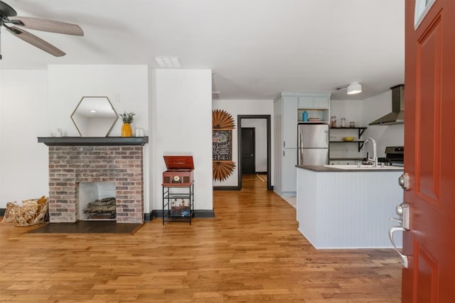 interior space with ceiling fan, open shelves, wall chimney exhaust hood, stainless steel appliances, and light wood-type flooring