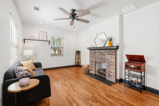 living area with wood finished floors, visible vents, a fireplace, and a ceiling fan