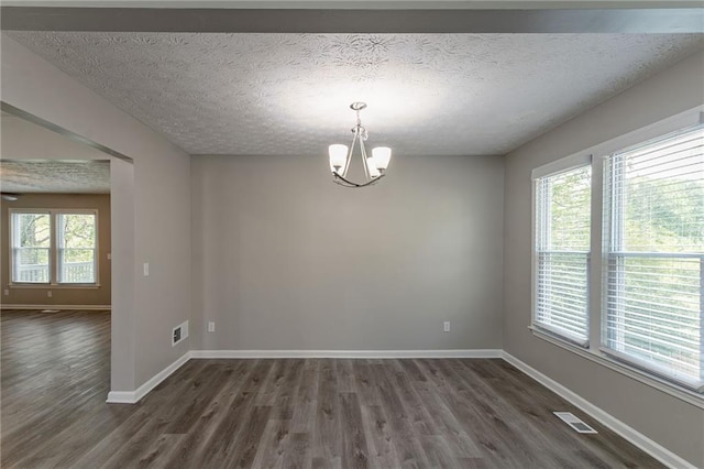 empty room with baseboards, a textured ceiling, a notable chandelier, and dark wood finished floors