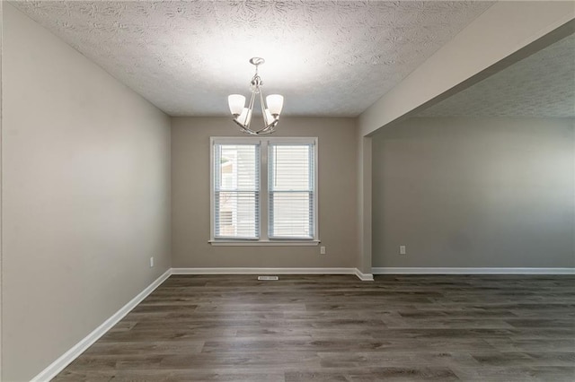 spare room with a textured ceiling, baseboards, dark wood-style flooring, and an inviting chandelier