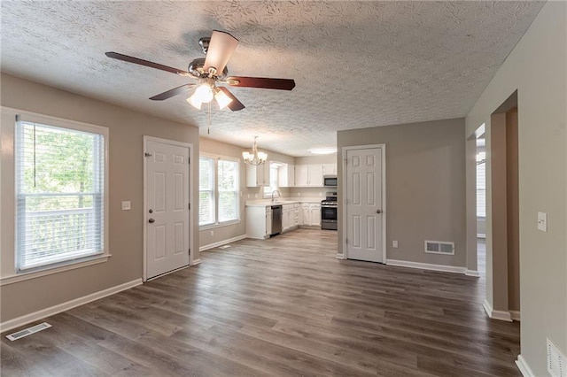unfurnished living room featuring a textured ceiling, visible vents, baseboards, and ceiling fan with notable chandelier