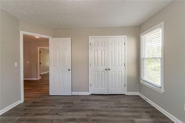 unfurnished bedroom featuring baseboards, a textured ceiling, a closet, and dark wood finished floors