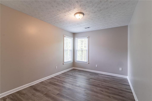 empty room with baseboards, visible vents, a textured ceiling, and dark wood-type flooring