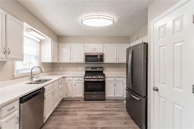 kitchen with light countertops, a sink, a textured ceiling, appliances with stainless steel finishes, and white cabinetry