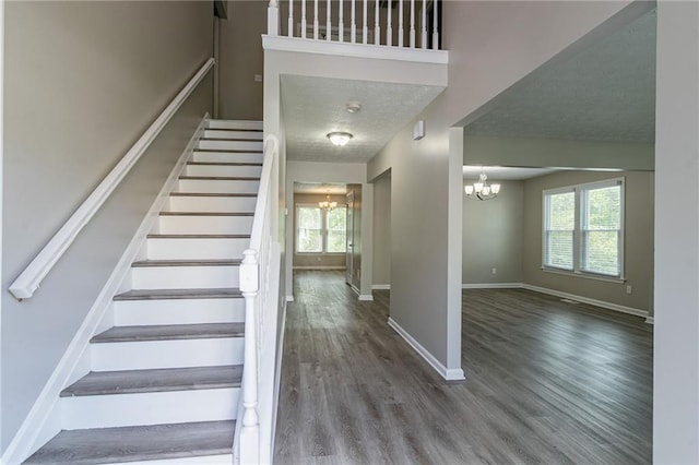 staircase featuring baseboards, wood finished floors, a chandelier, and a textured ceiling