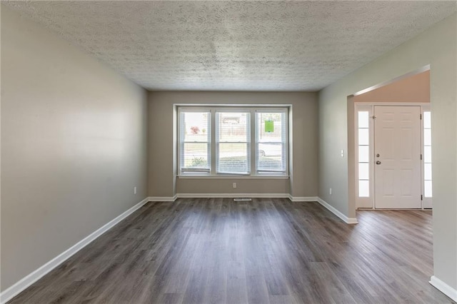 spare room featuring dark wood-type flooring, a textured ceiling, and baseboards