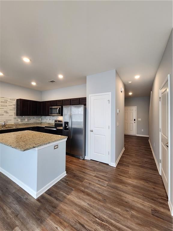 kitchen with light stone countertops, appliances with stainless steel finishes, a center island, and dark wood-type flooring