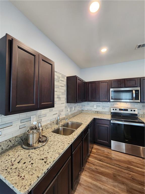 kitchen with dark brown cabinetry, sink, stainless steel appliances, light stone countertops, and hardwood / wood-style floors