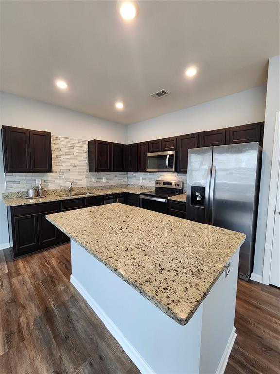 kitchen featuring appliances with stainless steel finishes, backsplash, dark hardwood / wood-style flooring, a center island, and light stone countertops