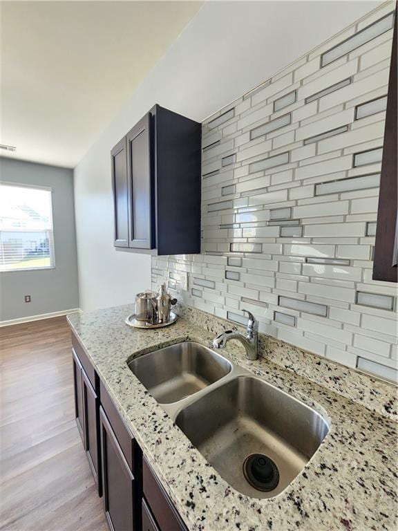 kitchen with sink, backsplash, light stone counters, dark brown cabinetry, and light wood-type flooring