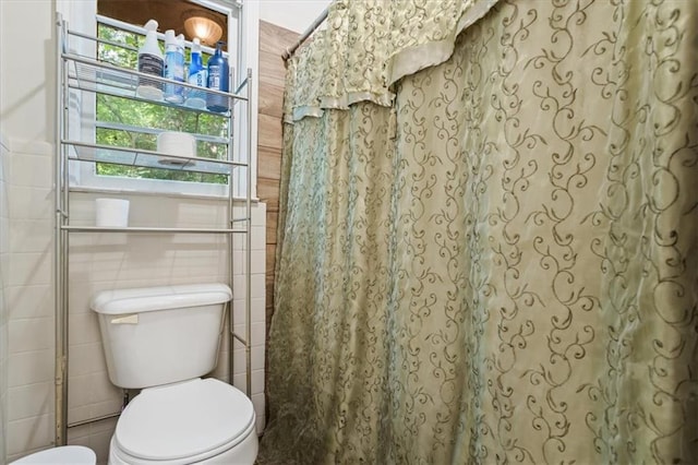 bathroom featuring toilet, tile walls, and a shower with shower curtain