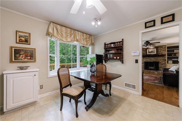 dining room with ceiling fan, a fireplace, baseboards, visible vents, and ornamental molding