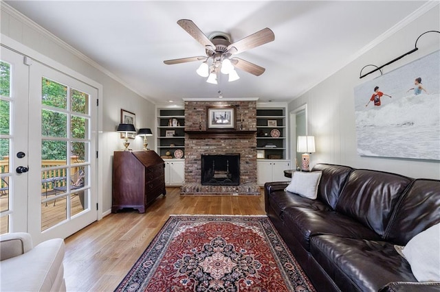 living room with ceiling fan, a brick fireplace, built in features, wood finished floors, and ornamental molding