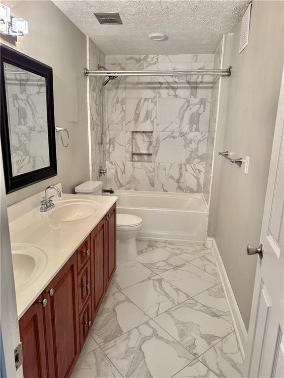 121 Brittany Ct, Duluth, GA 30096 - bathroom featuring a textured ceiling, double vanity, toilet, washtub / shower combination, and baseboards