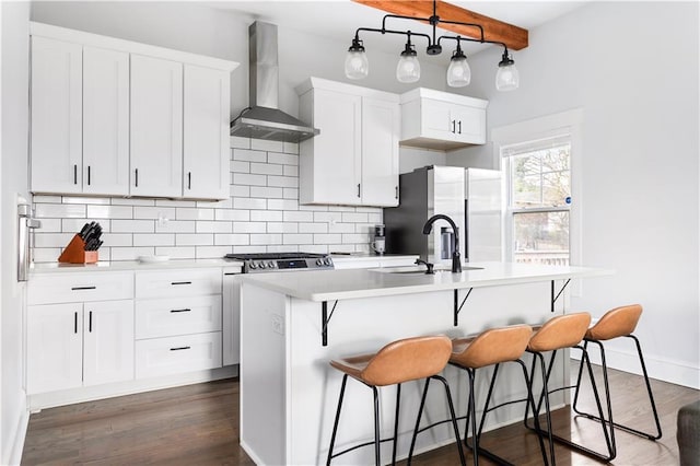kitchen with wall chimney exhaust hood, stainless steel fridge, an island with sink, decorative backsplash, and beam ceiling