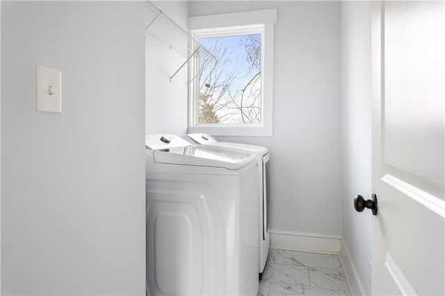 washroom featuring washer and dryer, light marble finish floors, and baseboards