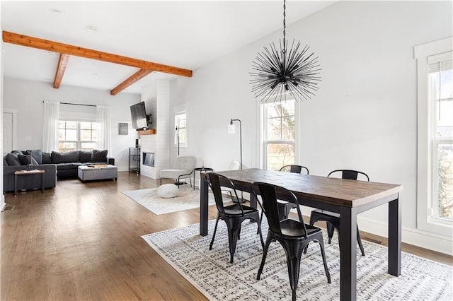 dining area featuring a chandelier, plenty of natural light, baseboards, wood finished floors, and beamed ceiling